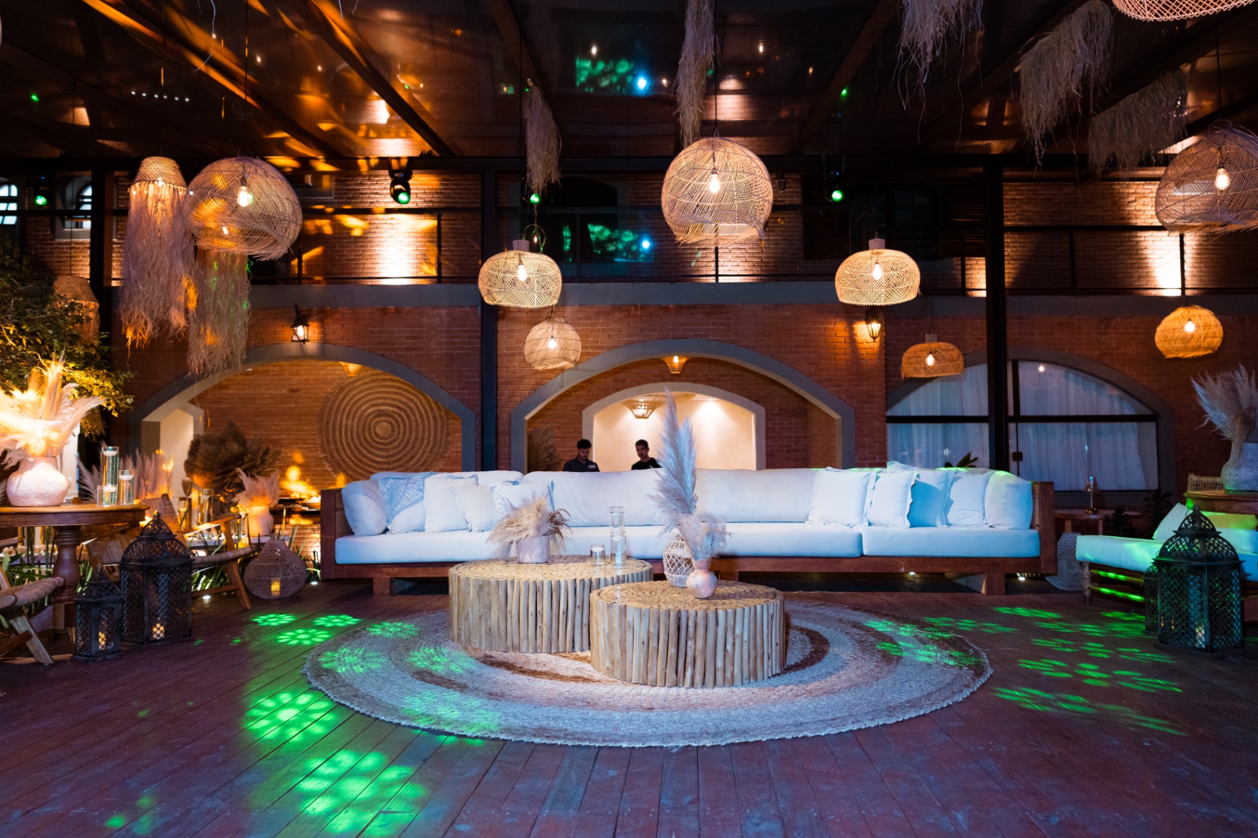 Lounge coberto com sofás claros, luminárias de palha e iluminação cênica