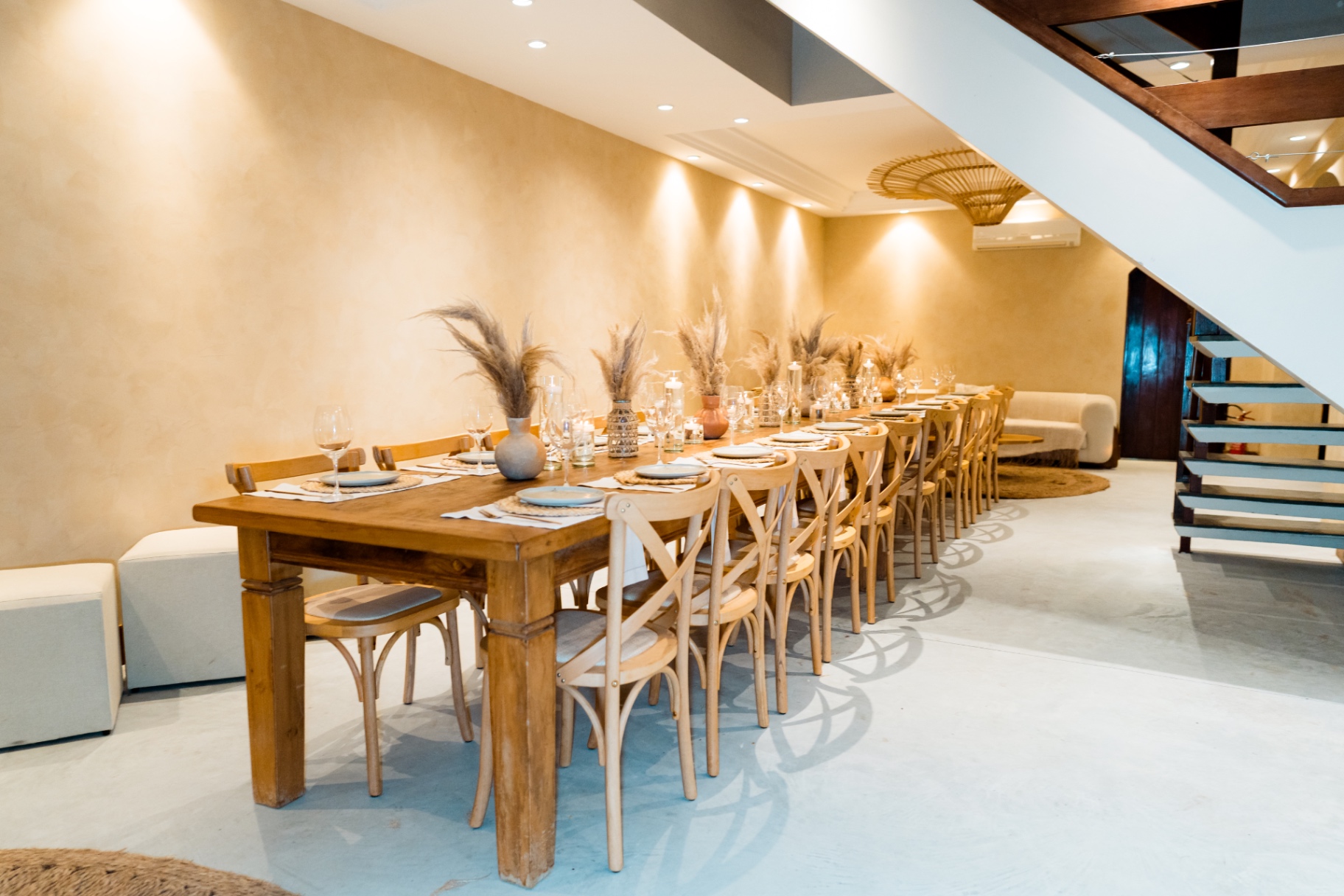 Salão interno com mesa longa de madeira posta e iluminação quente